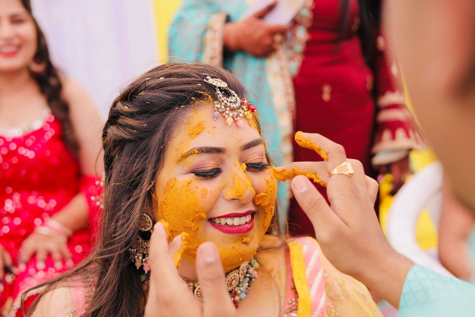 A thick turmeric paste being applied to a young woman's face — the Indian haldi ceremony
